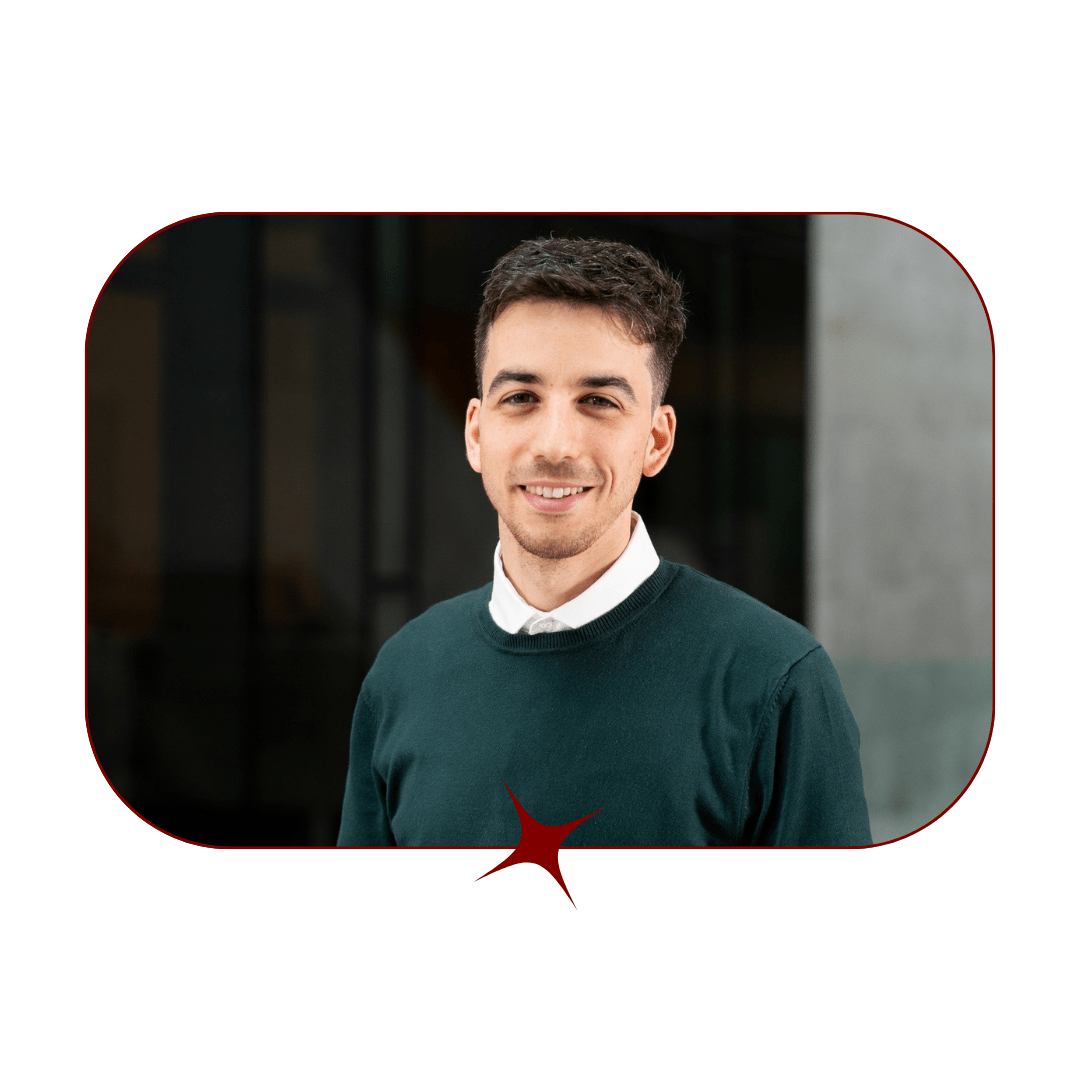 Picture of a young, smiling, dark-haired man wearing a dark green sweater and white mock-neck in front of a blurred background. The picture is bordered by a thin, red-lined frame with a red star in the center. 