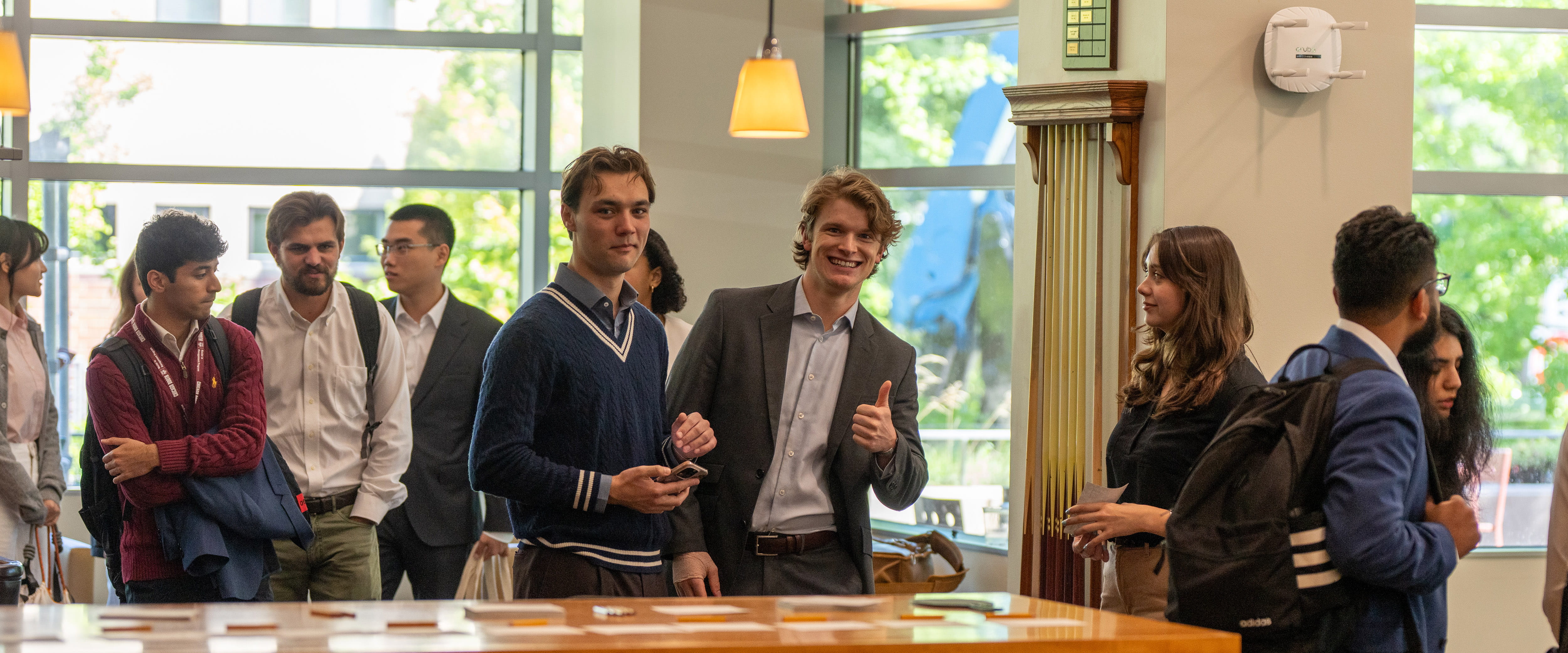 Two students with a group of others, smiling at the camera with a thumbs up, during First Day.