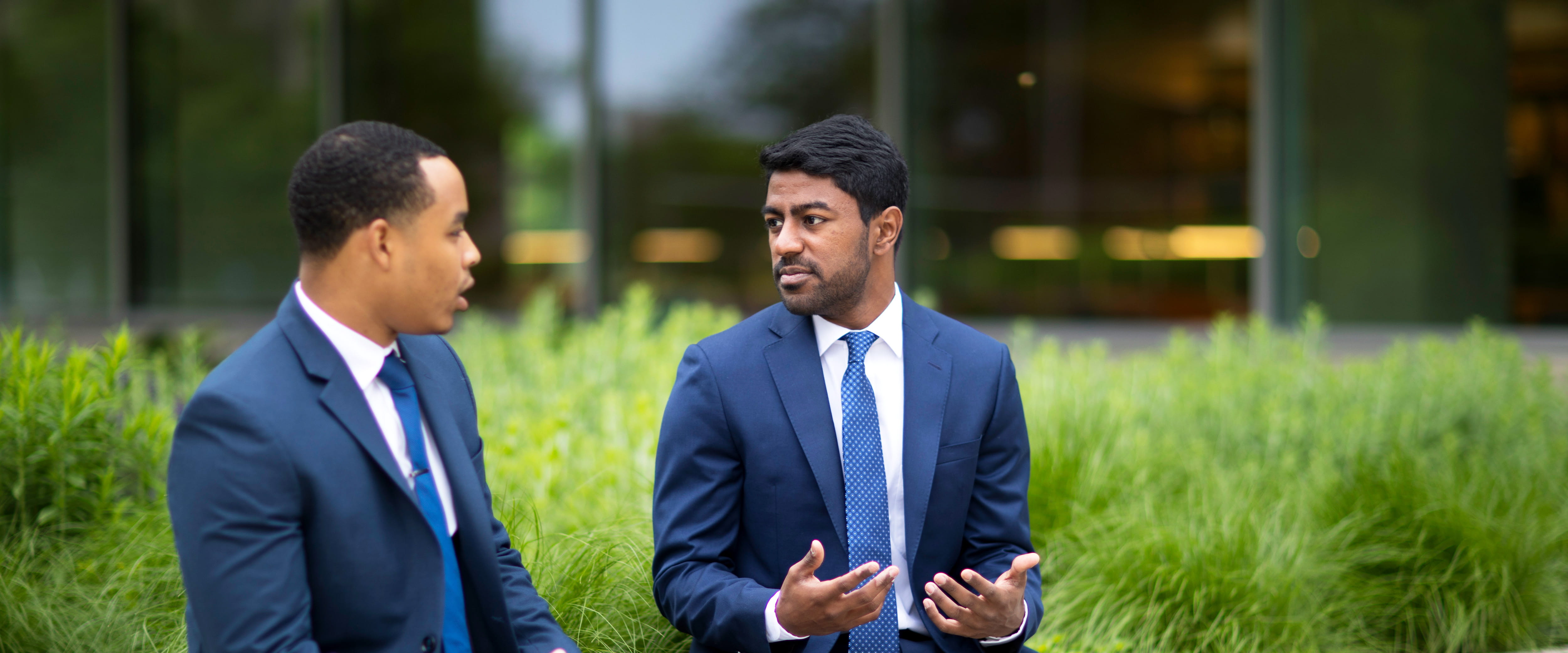 Two students in suits have a conversation while sitting in front of Harper Center.
