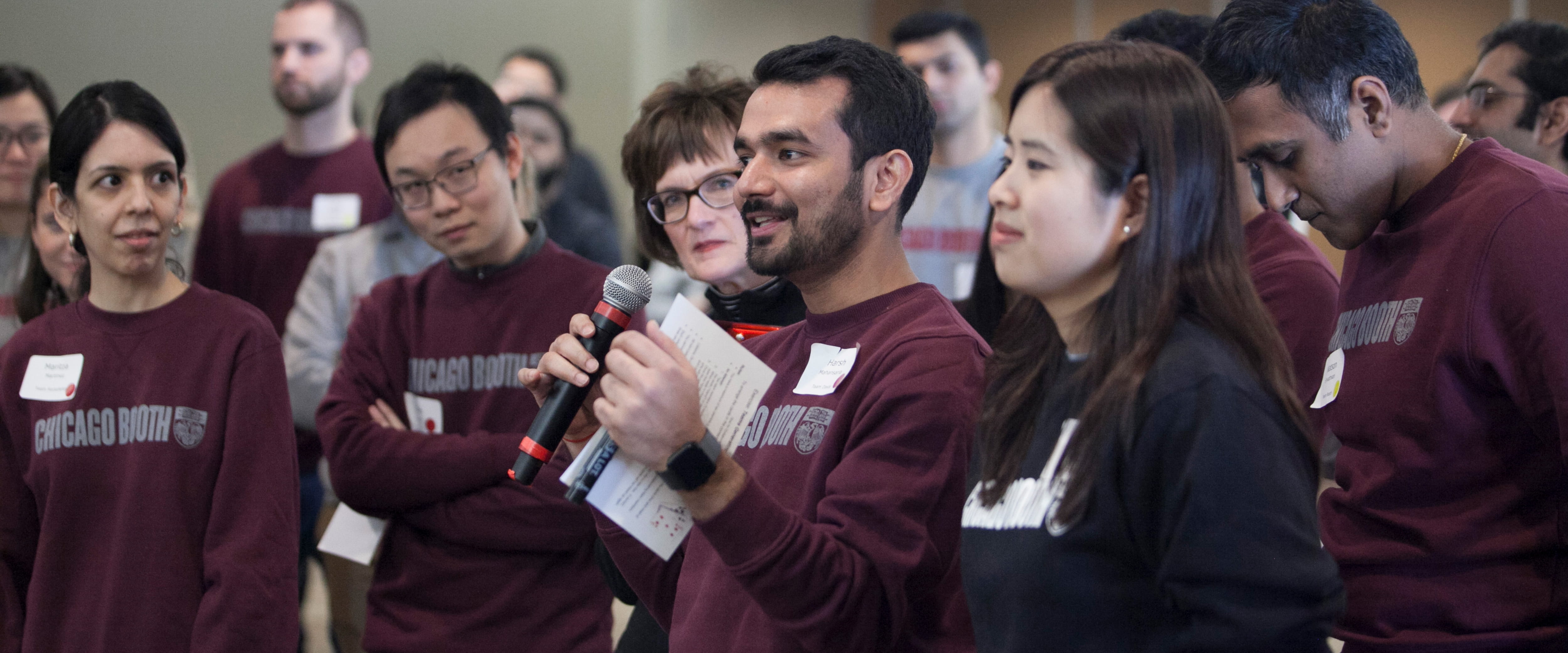 Man speaking into a microphone with students participating in a leadership course. 
