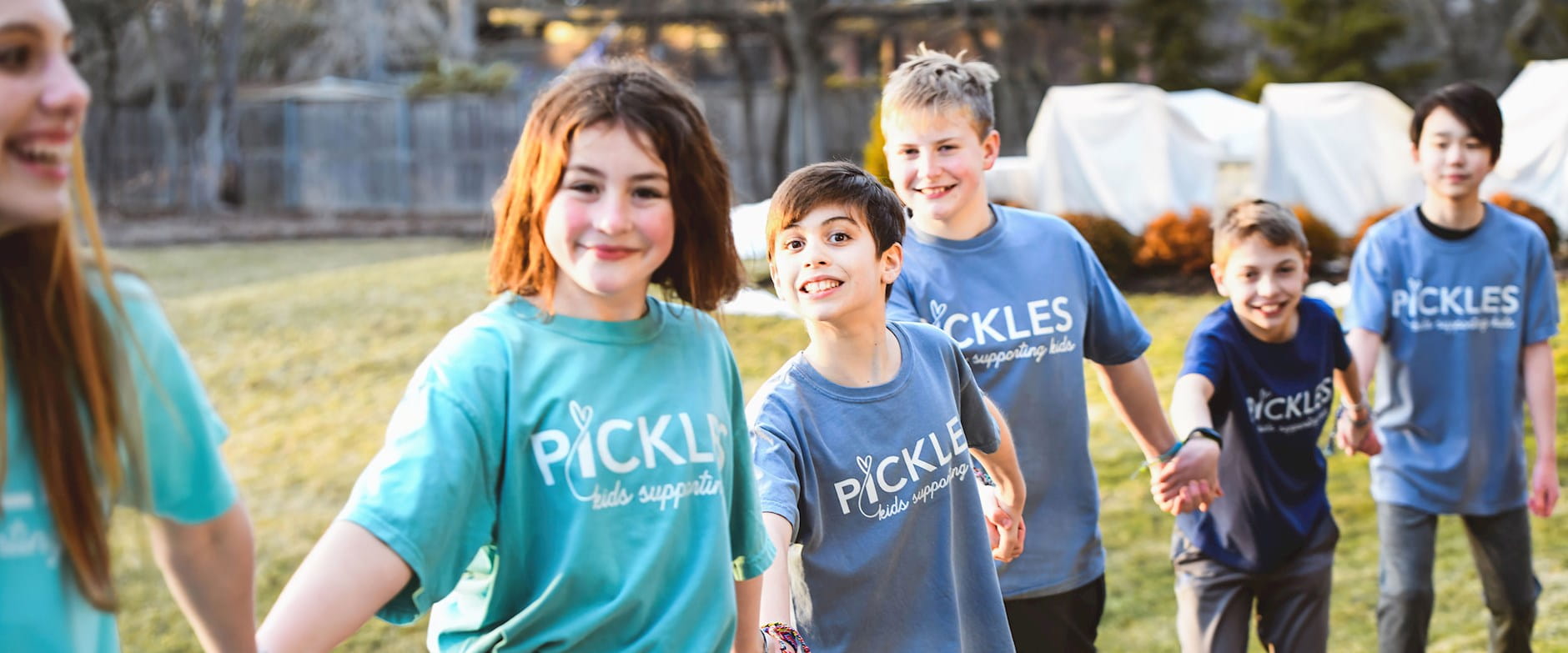 Kids a part of the Pickles Group organization join hands and smile outside