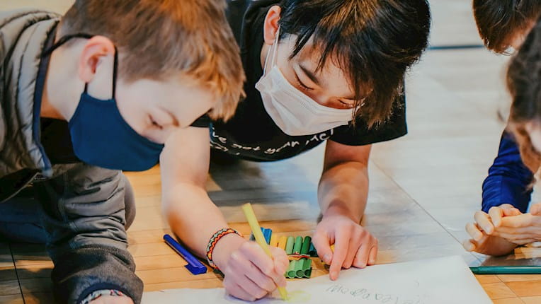 Kids from the Pickles Group indoors coloring while wearing masks