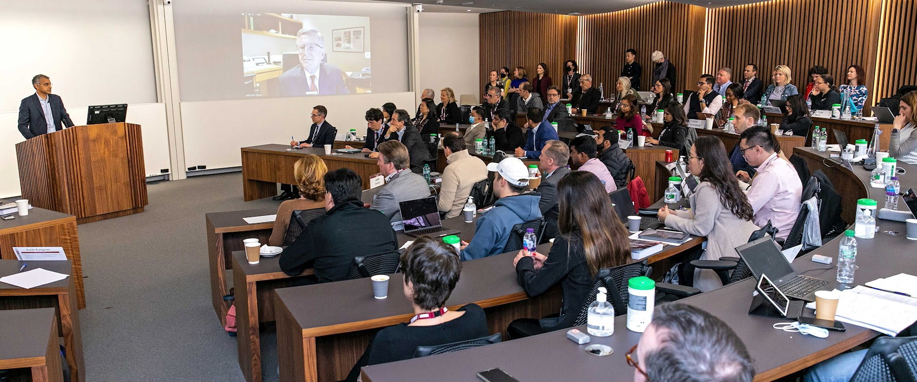 Madhav Rajan speaks at the podium of a London Campus classroom during the London Grand Opening