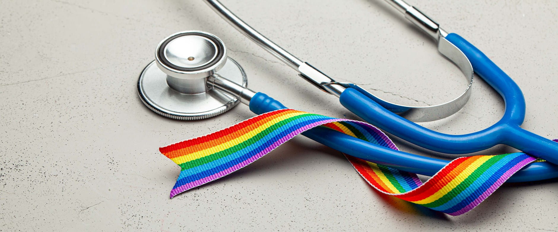 Stethoscope laying on a surface wrapped in an LGBTQIA+ rainbow ribbon