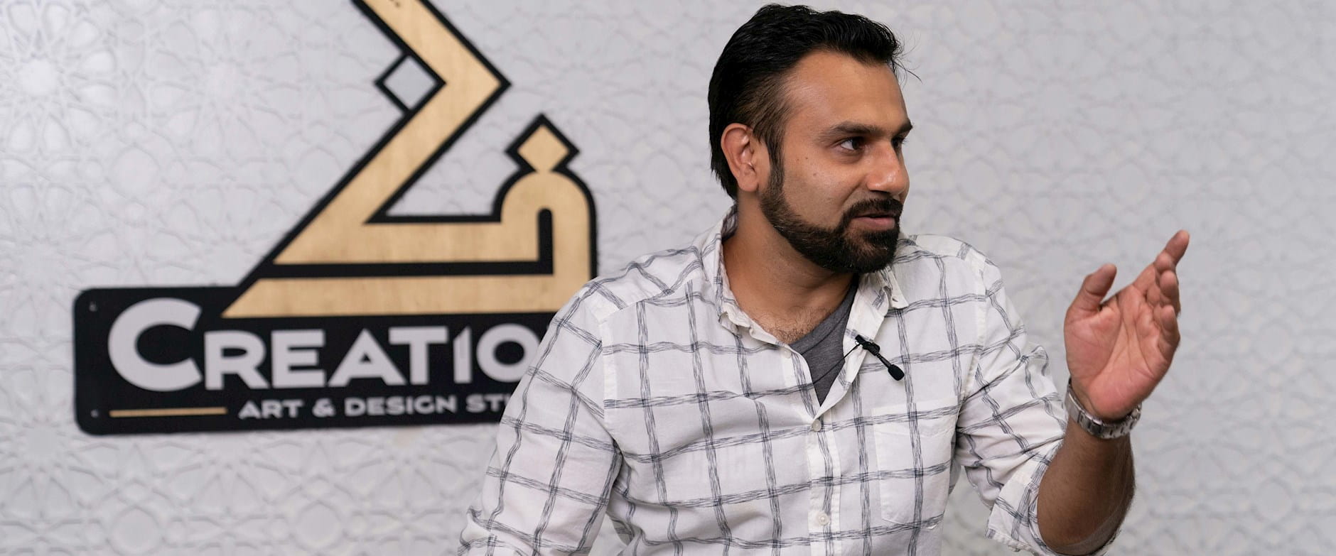 Zeeshan Farooq speaking in front of a sign for his "CreationZ" Art & Design Studio