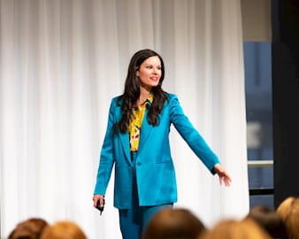 Erin Diehl speaking on stage in a blue suit