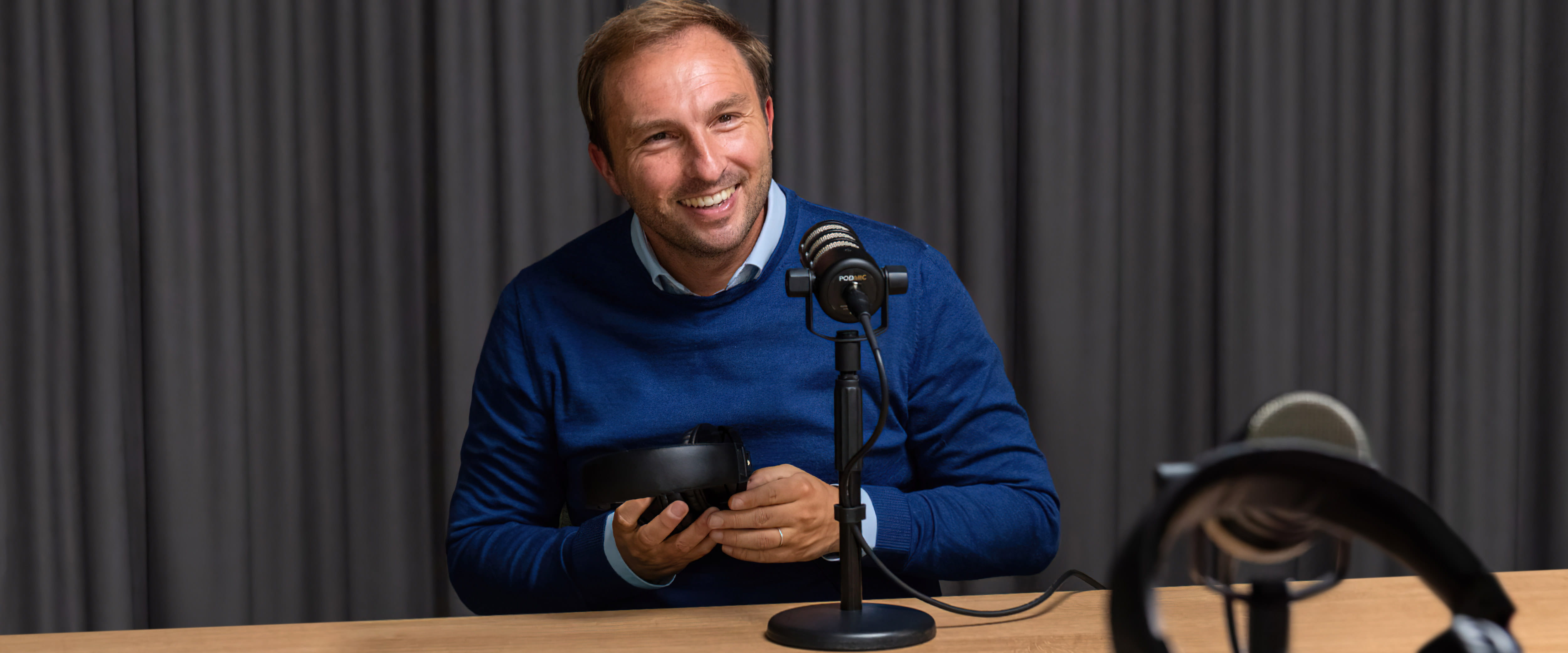 Guy Van Neck smiling in front of a microphone and about to put on headphones at an interview