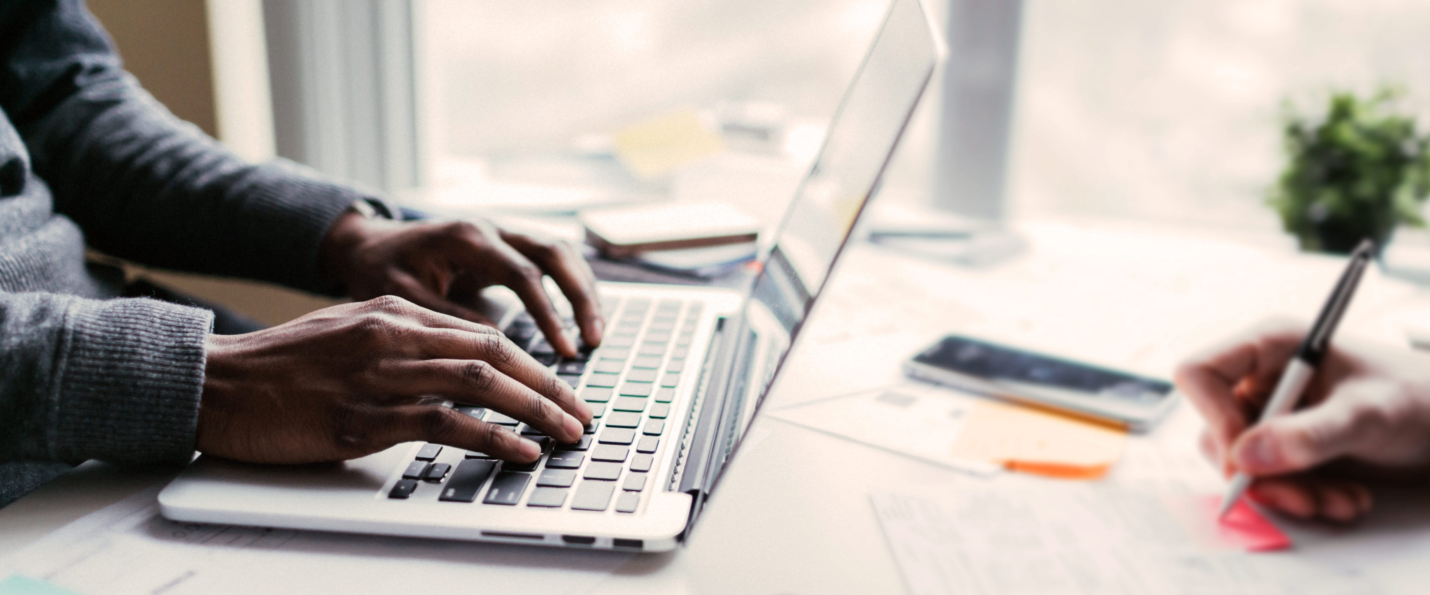 Man's hands on a laptop sharing a desk with a woman writing notes