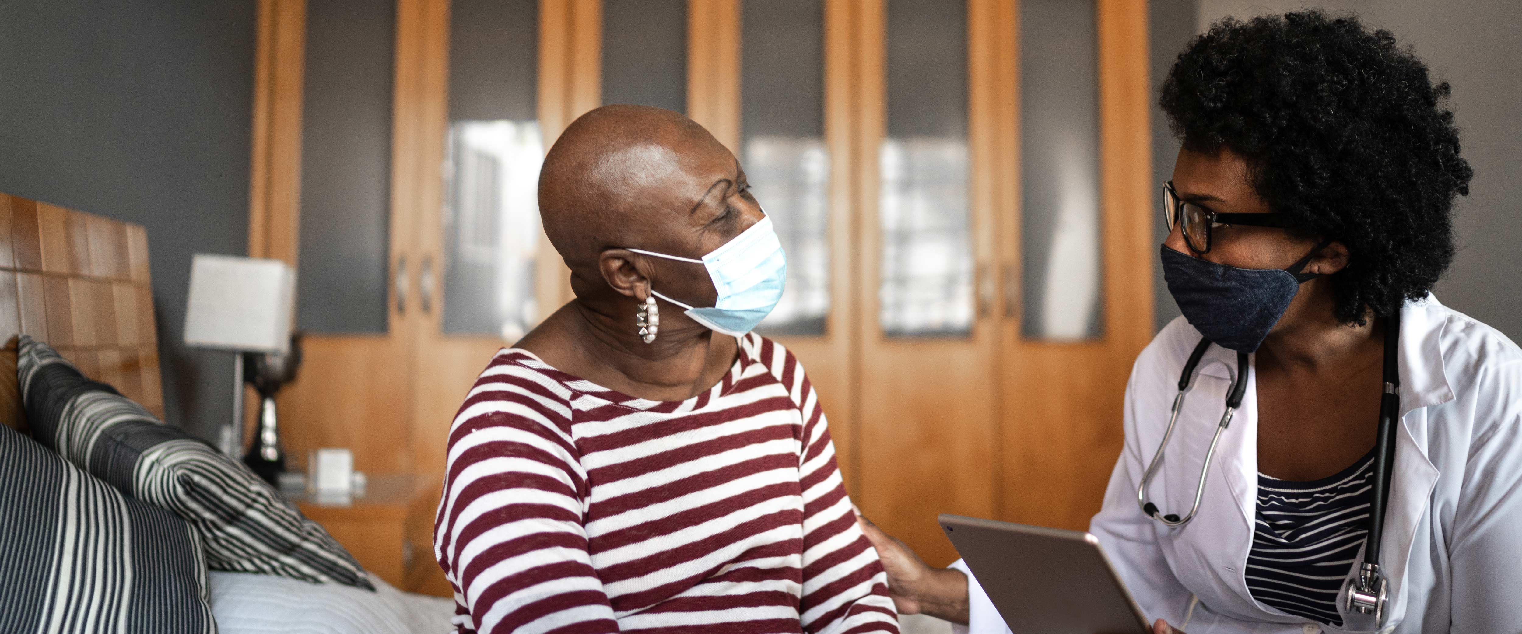 A doctor wearing a mask and using a tablet during a check-up appointment with a masked patient