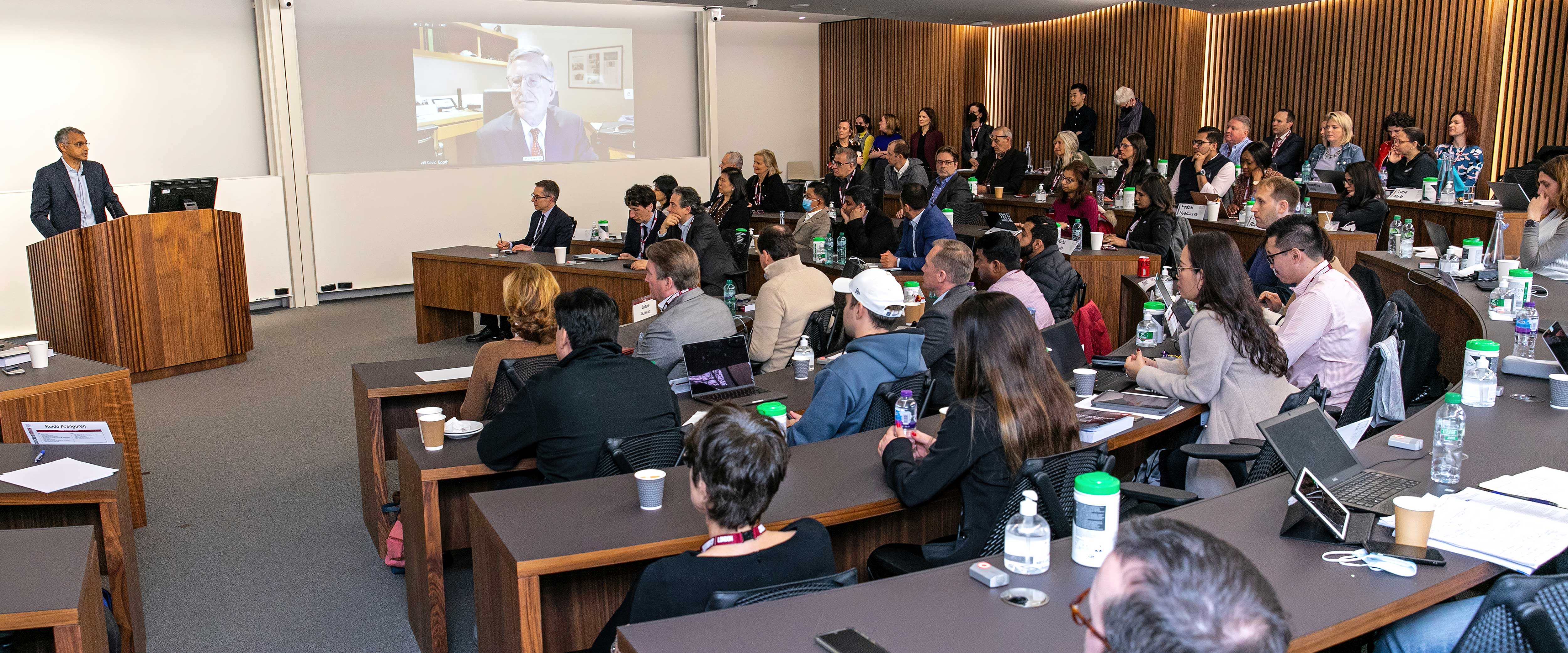 Madhav Rajan speaks at the podium of a London Campus classroom during the London Grand Opening