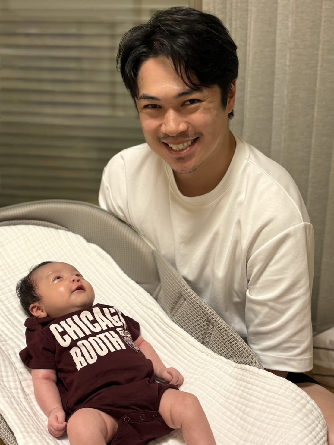 A man smiling and a baby wearing a Chicago Booth onesie