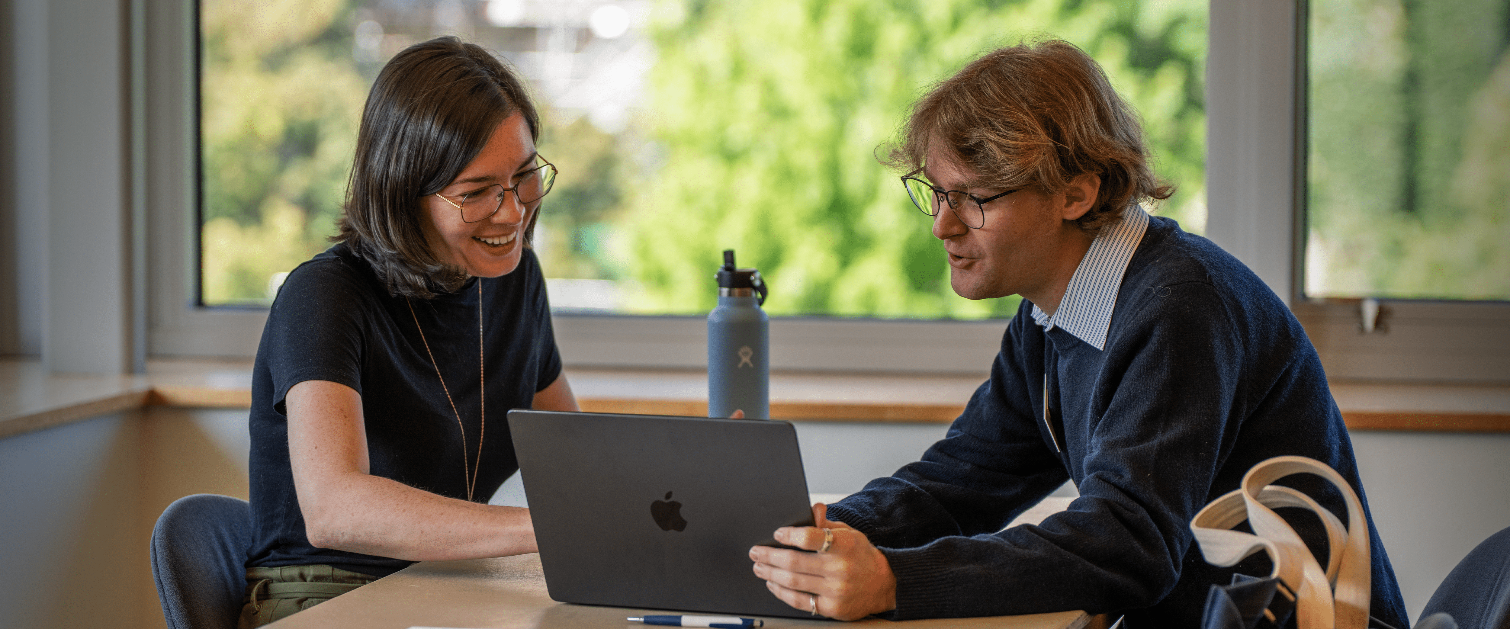 Two people talking and looking at a laptop.