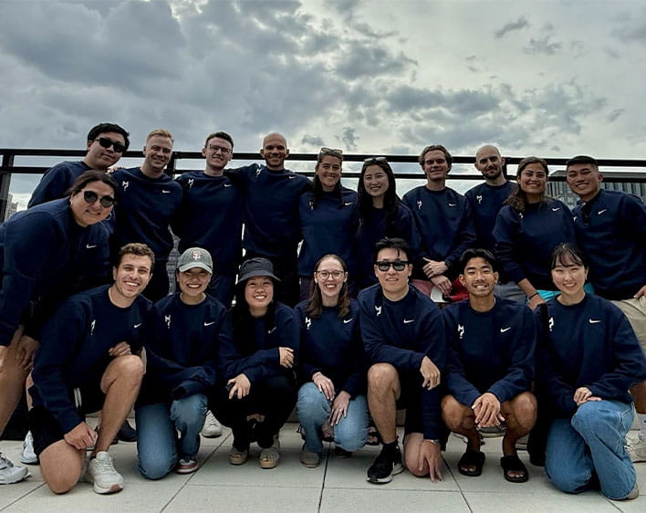 Patrick with a group of 16 plus Boothies smiling in matching navy shirts outside 