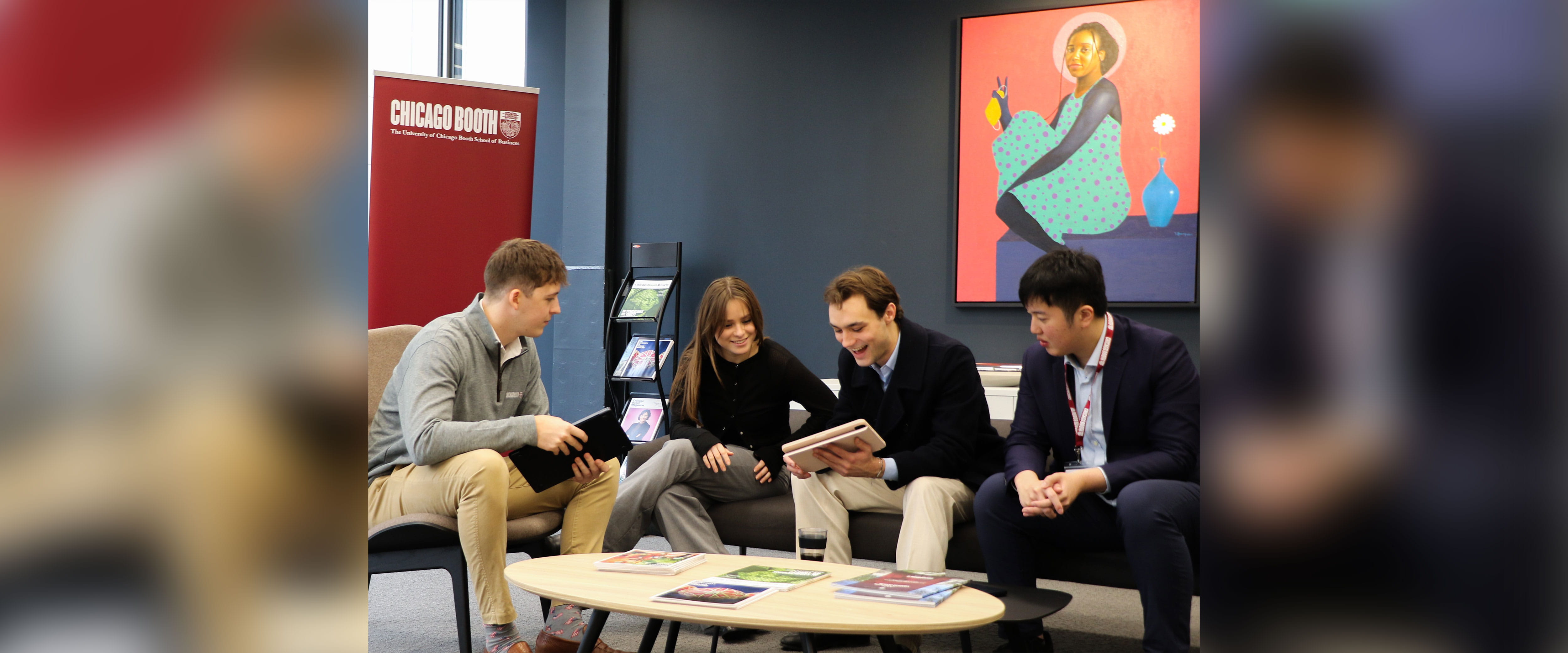 four students talking on couch while looking at tablet