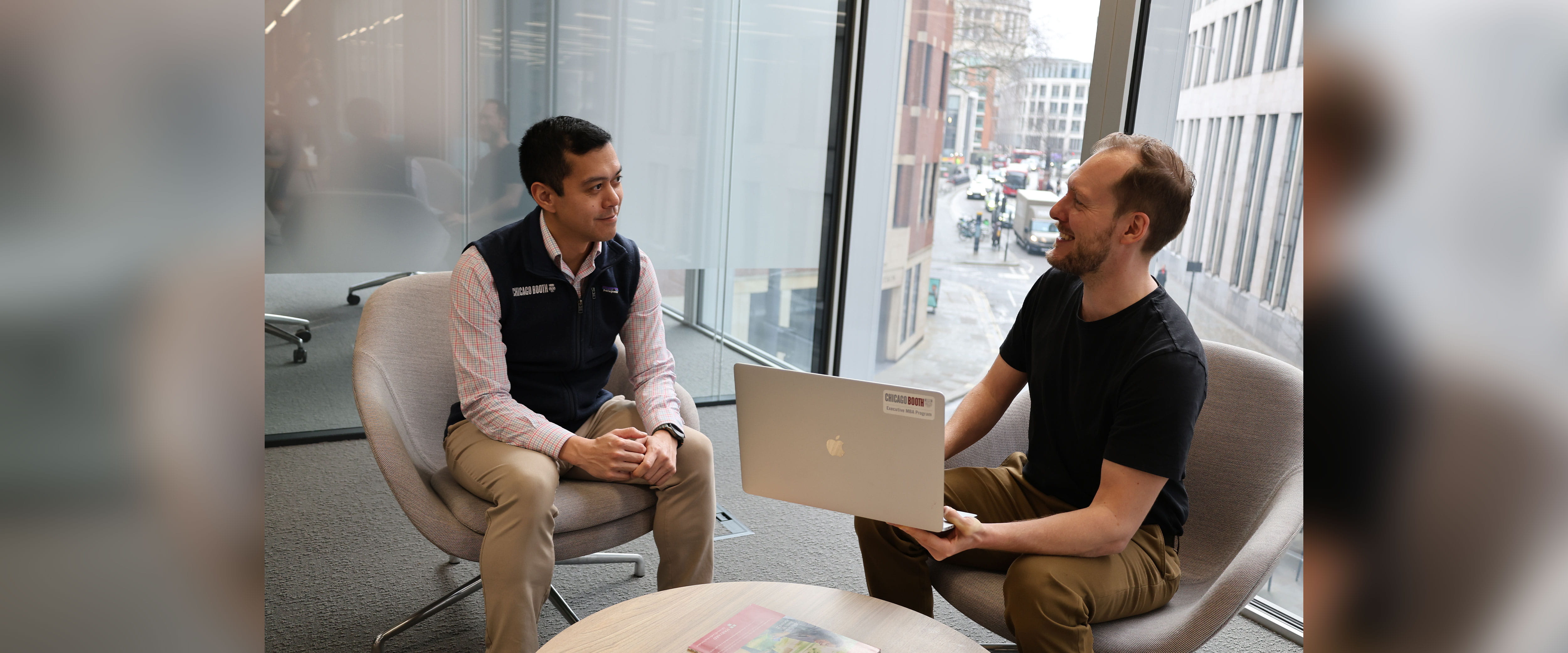 two EMBA students talking while sitting down with one student holding laptop