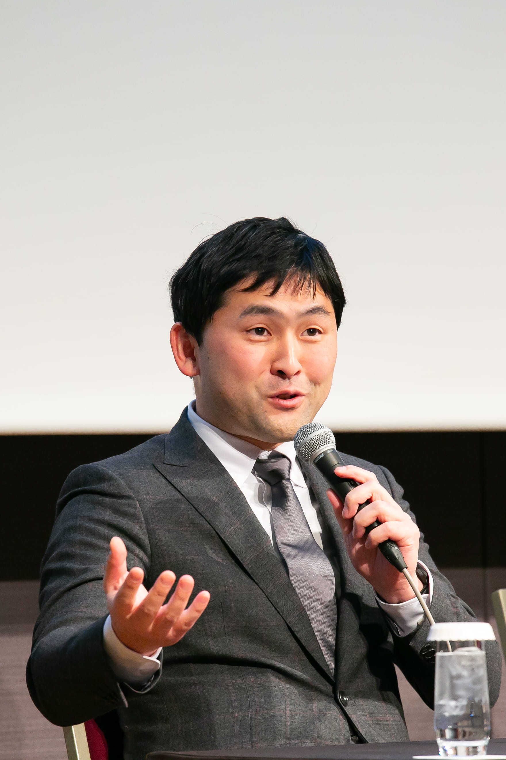 A man with dark hair wearing a suit talking into a microphone