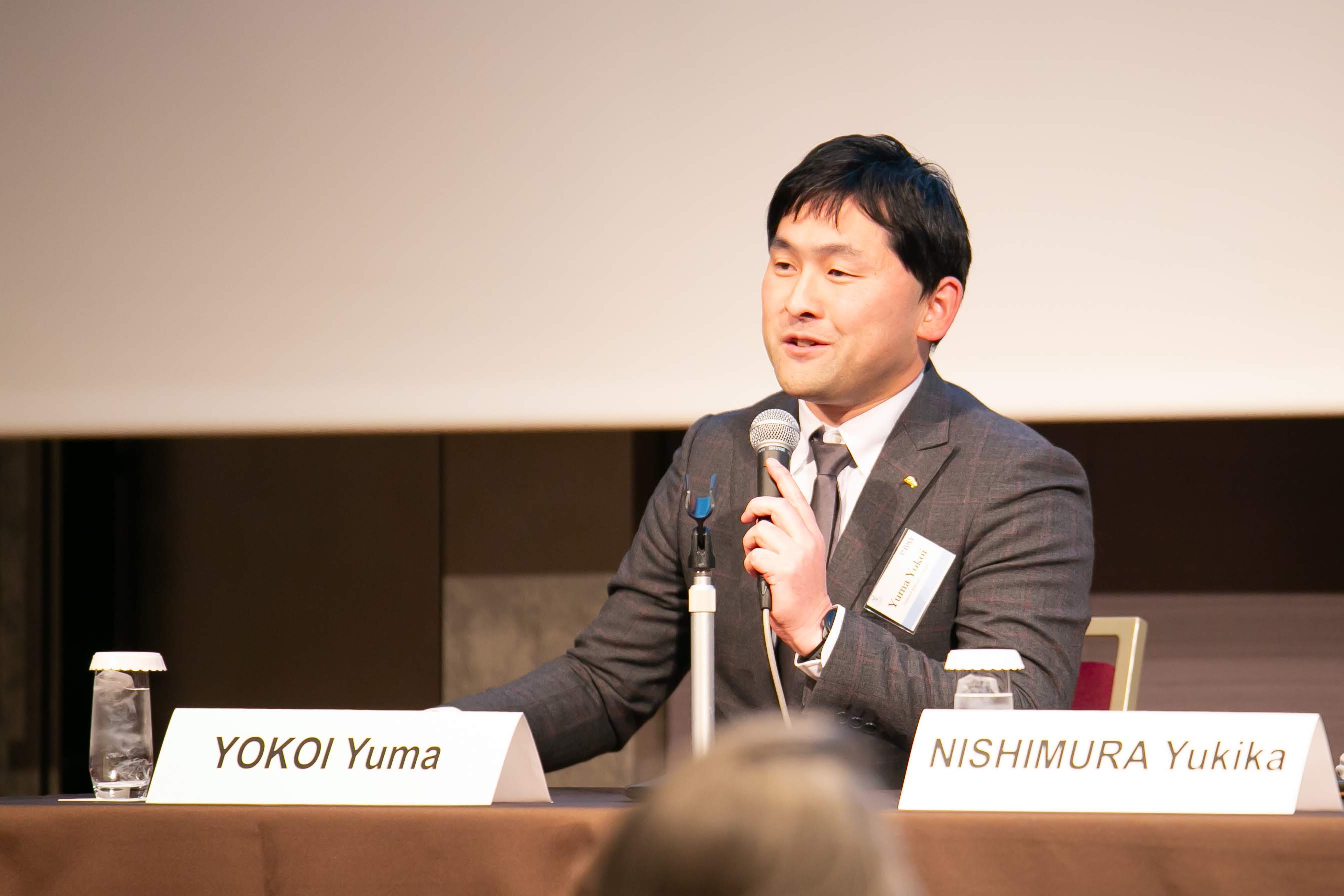 A man with dark hair wearing a suit speaking into a microphone