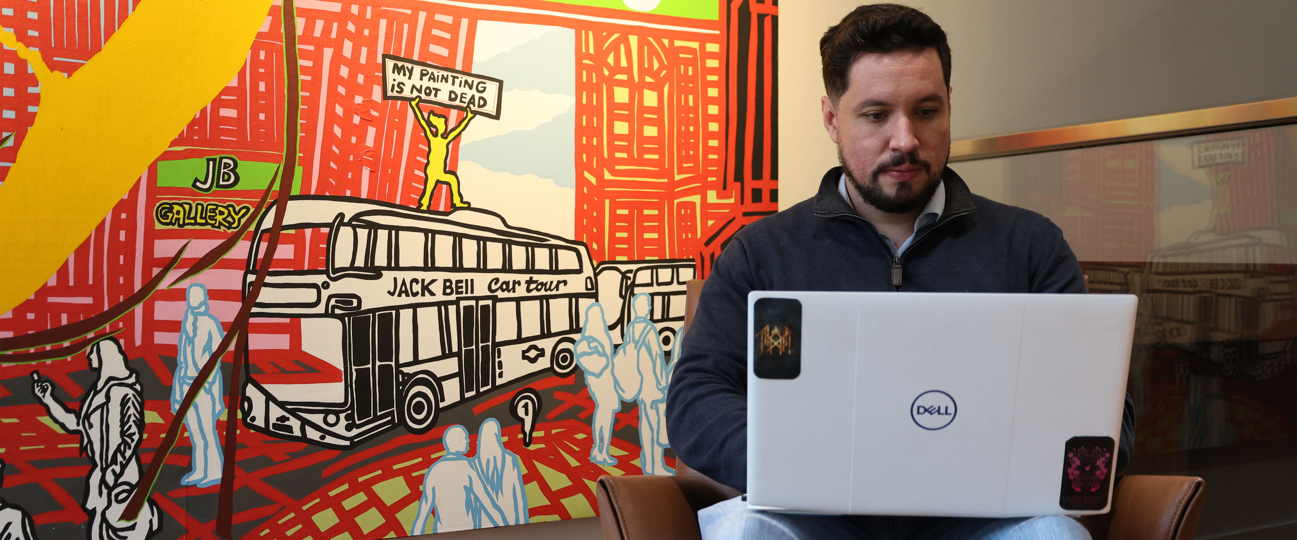 Caio Furtado Borges on laptop sitting down in front of artwork