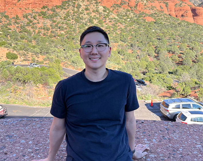 David Kim outside sitting on rock with mountains in the background
