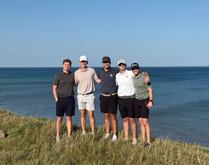 Mayes Lane with four friends outside in front of water standing in grass