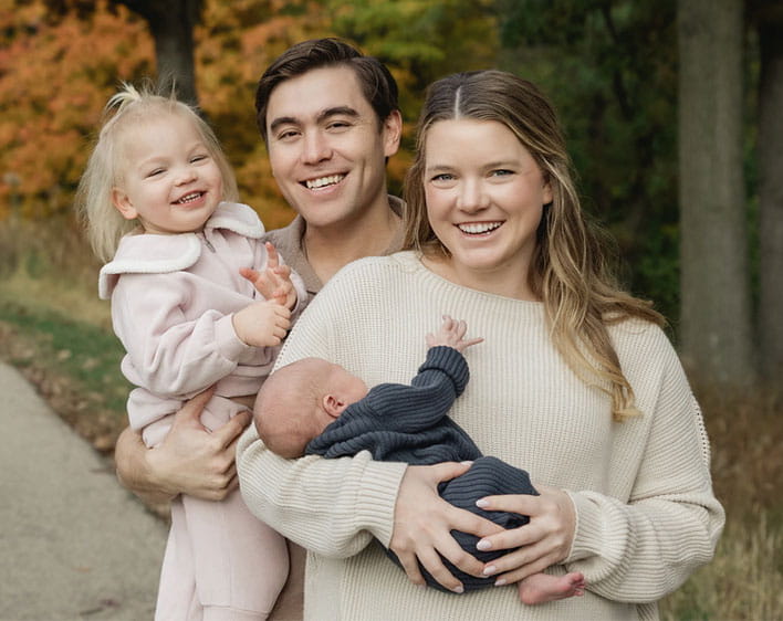 Madison Davis with her husband and two kids smiling with fall trees in background
