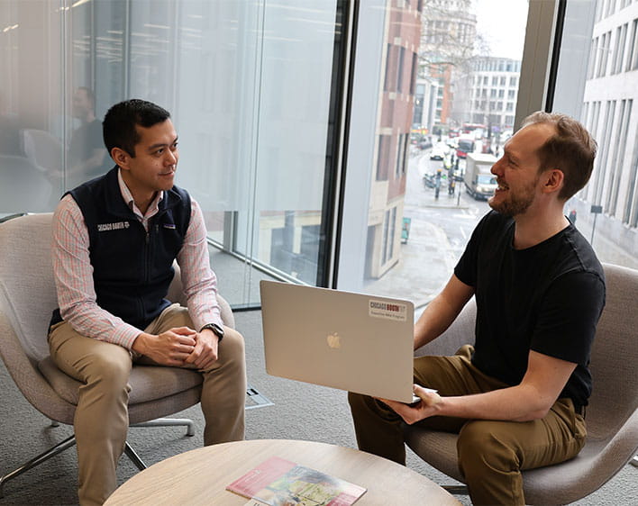 Booth students, Philipp Gschoepf and John Fabros sitting down at table conversing with laptop 