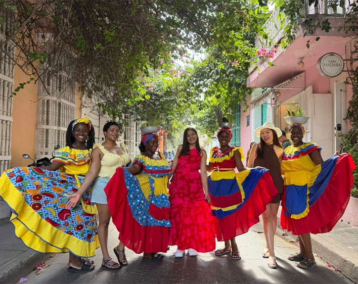 Ude Adekunle with women in Colombia wearing colorful gowns and holding fruit
