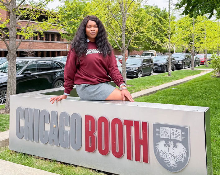 Ude Adekunle sitting on top of Chicago Booth sign outside of the Harper Center