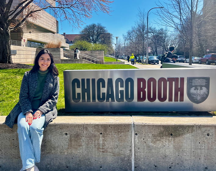 Camila Parra Ochoa sitting outside Harper Center by Chicago Booth sign