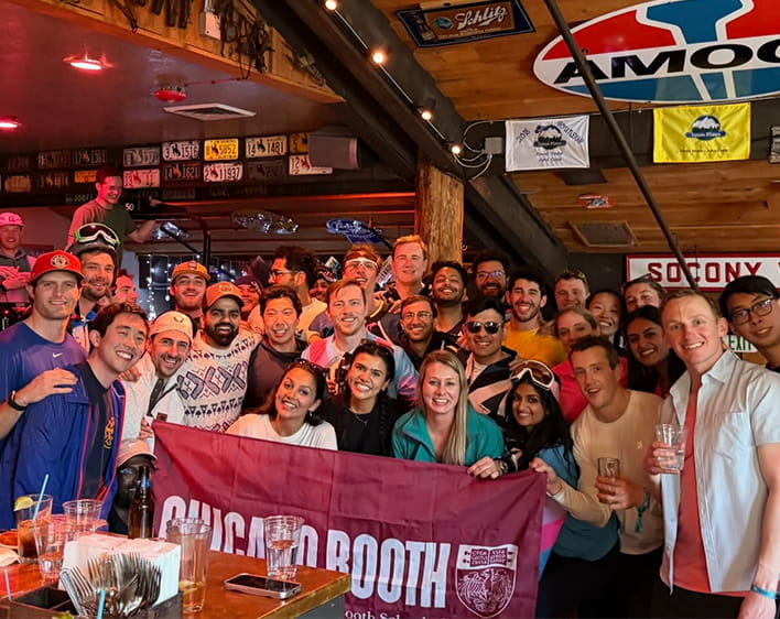 large group of Boothies with people in front holding up Booth Flag at annual ski trip