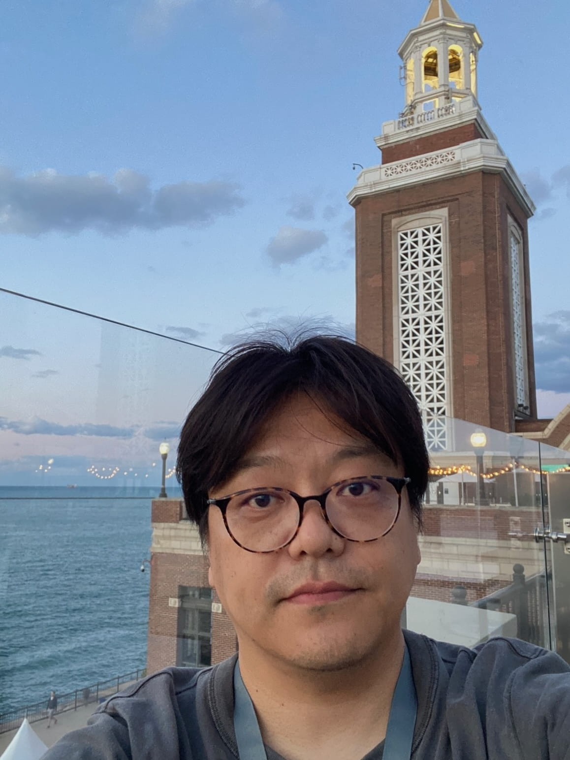 A man with glasses looking at the camera with a lake and a tower in the background