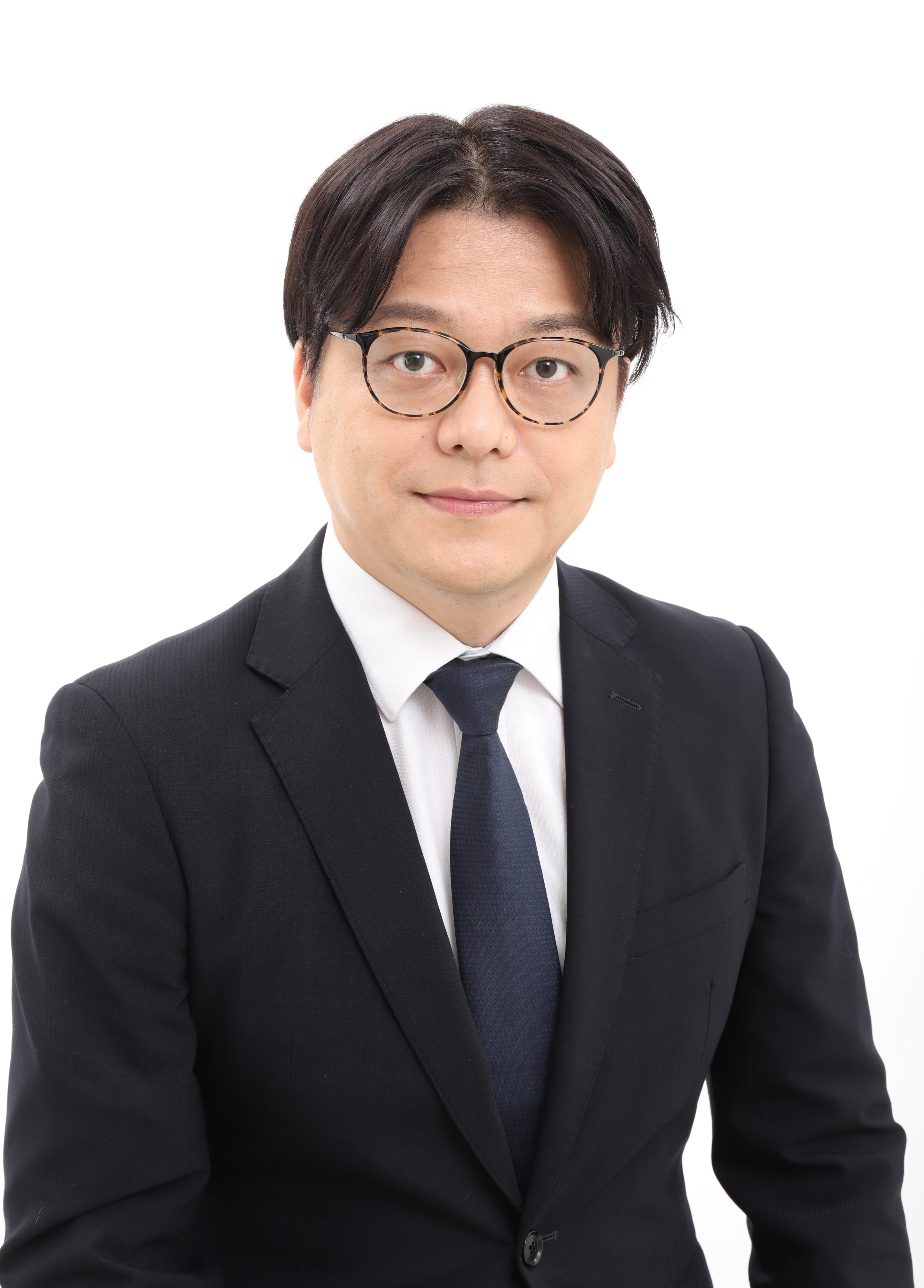 A man wearing glasses and a dark suit looking at the camera