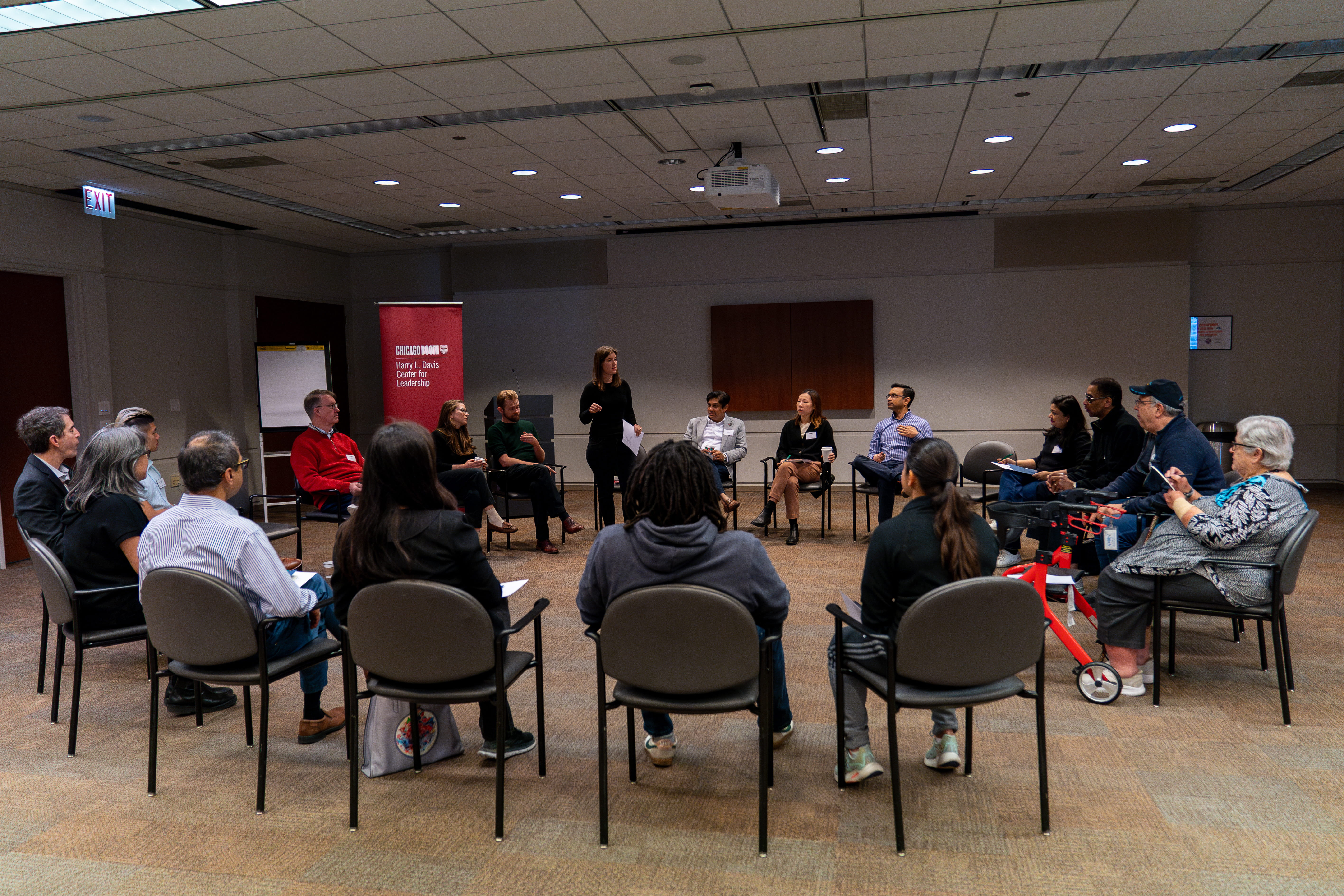 Group of many Booth alumni gathered seated in a circle at Gleacher Center