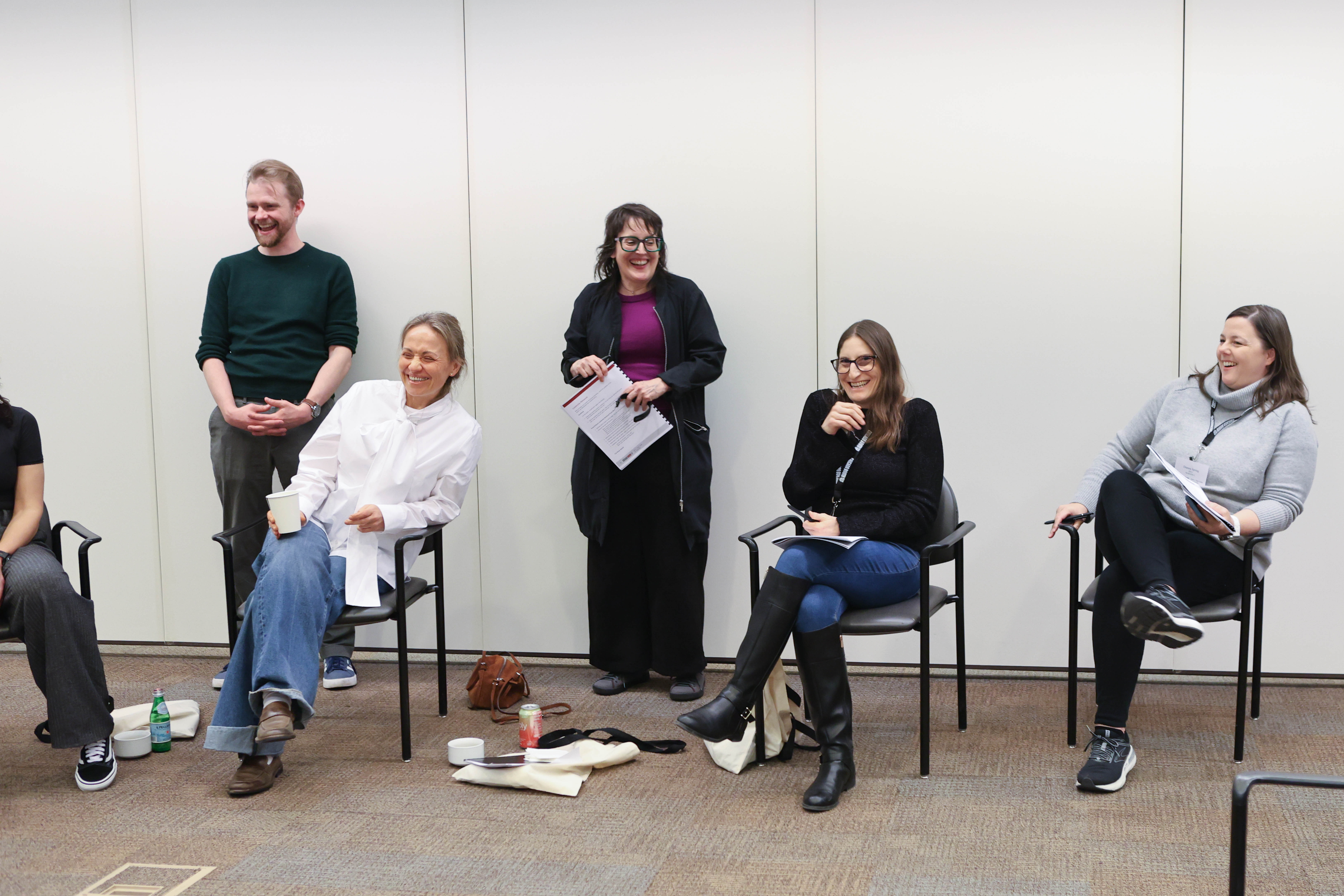 Chicago Booth alumni and coaches sitting and standing near a wall laughing 